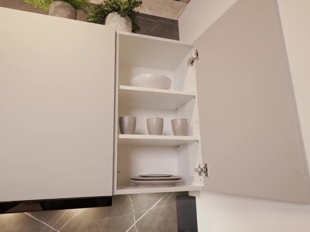 Geöffneter Oberschrank einer DAN FIRST Küche mit Geschirr